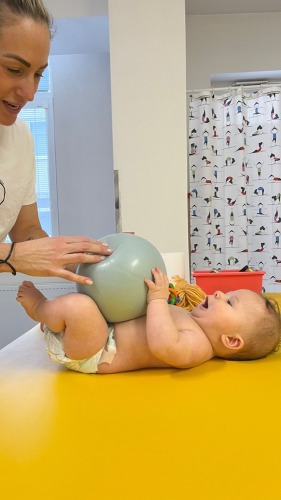 Fyzioterapeutka pri cvičení s bábätkom s lopticou na žltom lehátku