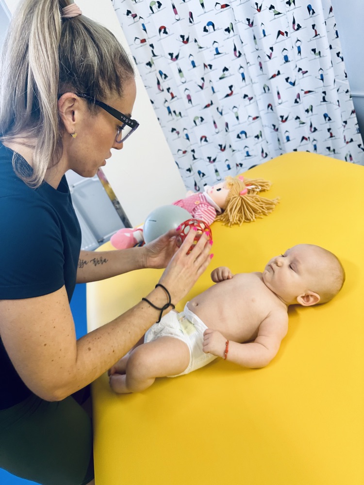 Fyzioterapeutka s bábätkom na žltom lehátku s hračkami